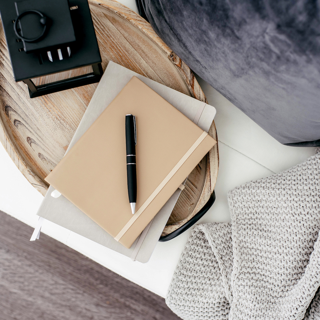 A notebook and pen on a tray on a bed.